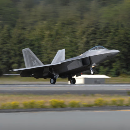 Gray fighter jet on a runway with green trees in the background