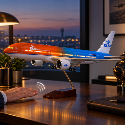 A KLM Royal Dutch Airlines model airplane on a wooden stand, displayed on a desk in an office setting with a person's hand near it.